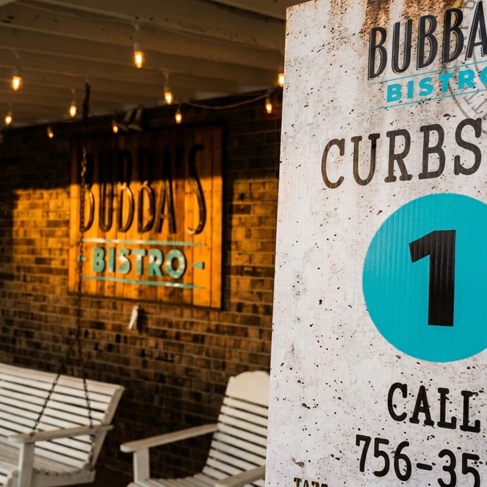 Bubba’s Bistro curbside pickup sign outside a warmly lit brick restaurant with white swing chairs.