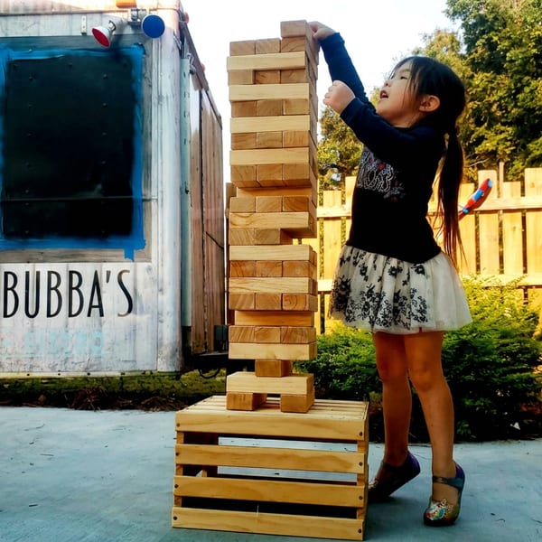 Child plays giant Jenga beside Bubba’s food trailer in an outdoor dining area.