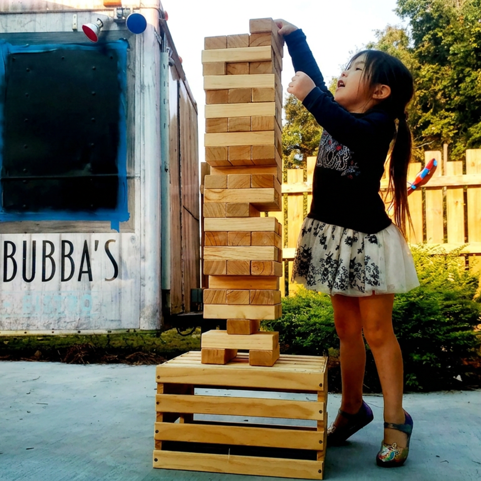 Child plays giant Jenga beside Bubba’s food trailer in an outdoor dining area.