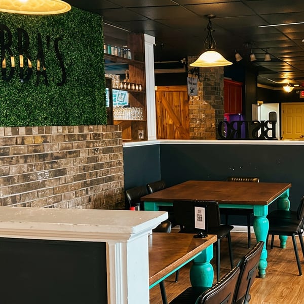 Rustic restaurant dining area with turquoise tables, exposed brick, wood-paneled walls, ceiling fans, and a large Birds sign.