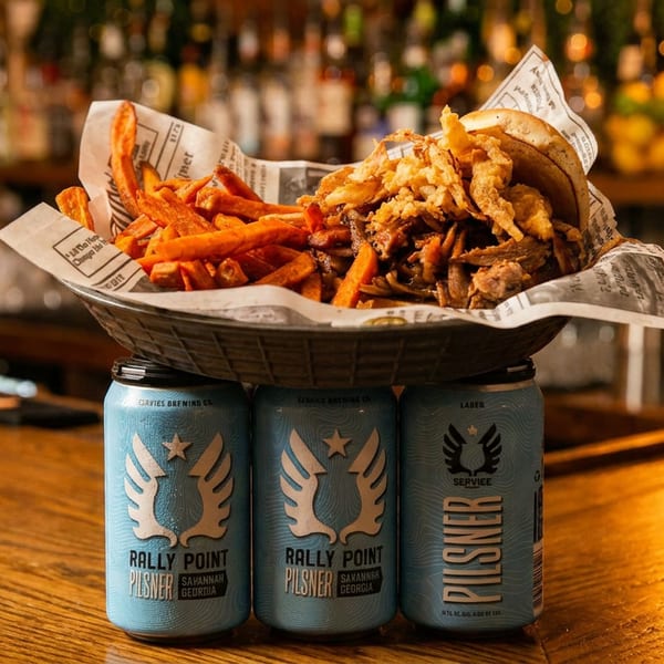 Basket of fries and crispy fried toppings balanced on three cans of Rally Point beer at a warmly lit bar.