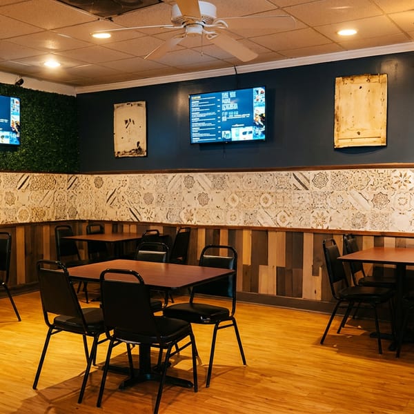 Warmly lit restaurant dining area with wooden tables, black chairs, patterned wall decor, and digital menu screens.