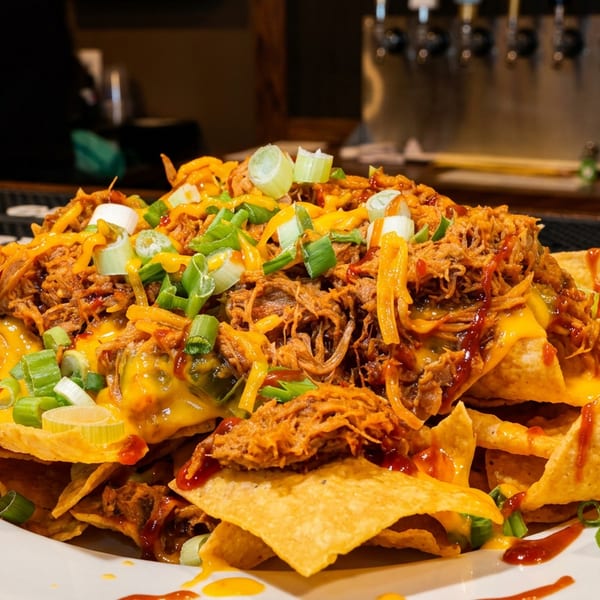 Loaded nachos topped with pulled meat, melted cheddar, green onions, and hot sauce beside a Texas Pete bottle.