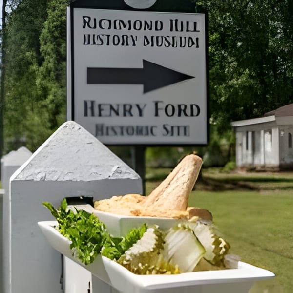 A white sign pointing to the "Richmond Hill History Museum" and "Henry Ford Historic Site" with food in the foreground.