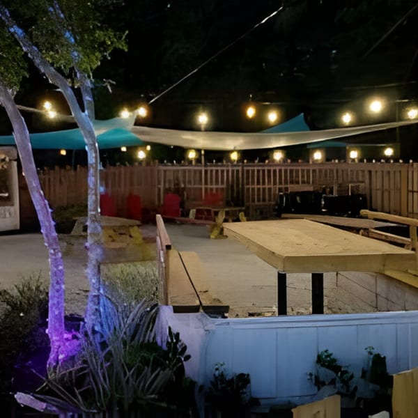 Bubba's Bistro outdoor patio at night, with string lights, wooden tables, and red chairs.