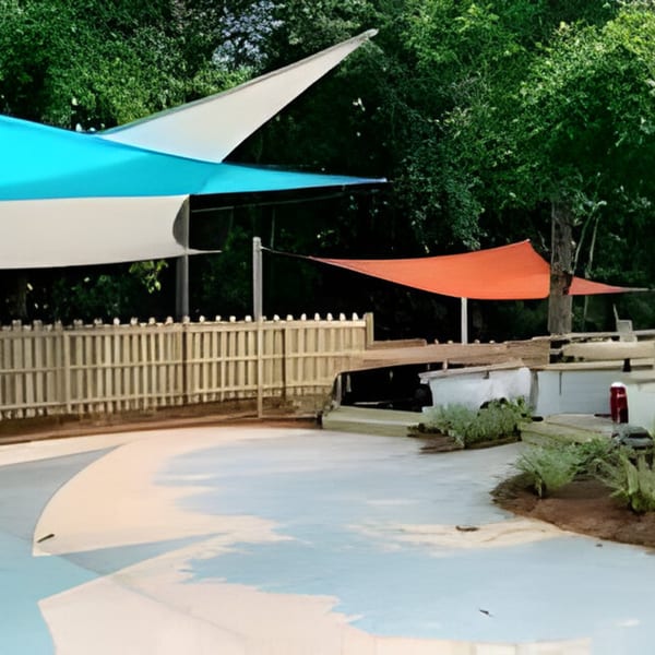 Bubba's Bistro outdoor patio with blue and orange shade sails, a wooden fence, and lush greenery.