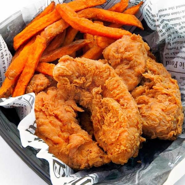 Crispy fried chicken tenders and sweet potato fries served in a basket lined with newspaper.