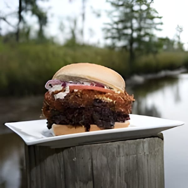 Bubba's Bistro's fried chicken sandwich with tomato and sauce, on a plate, on a wooden post by water.