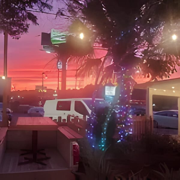 Bubba's Bistro patio at sunset with string lights, palm trees, and a vibrant red sky.