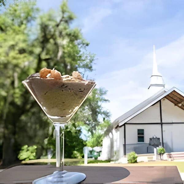 A Bubba's Bistro dessert in a martini glass, with a white church and trees in the background.